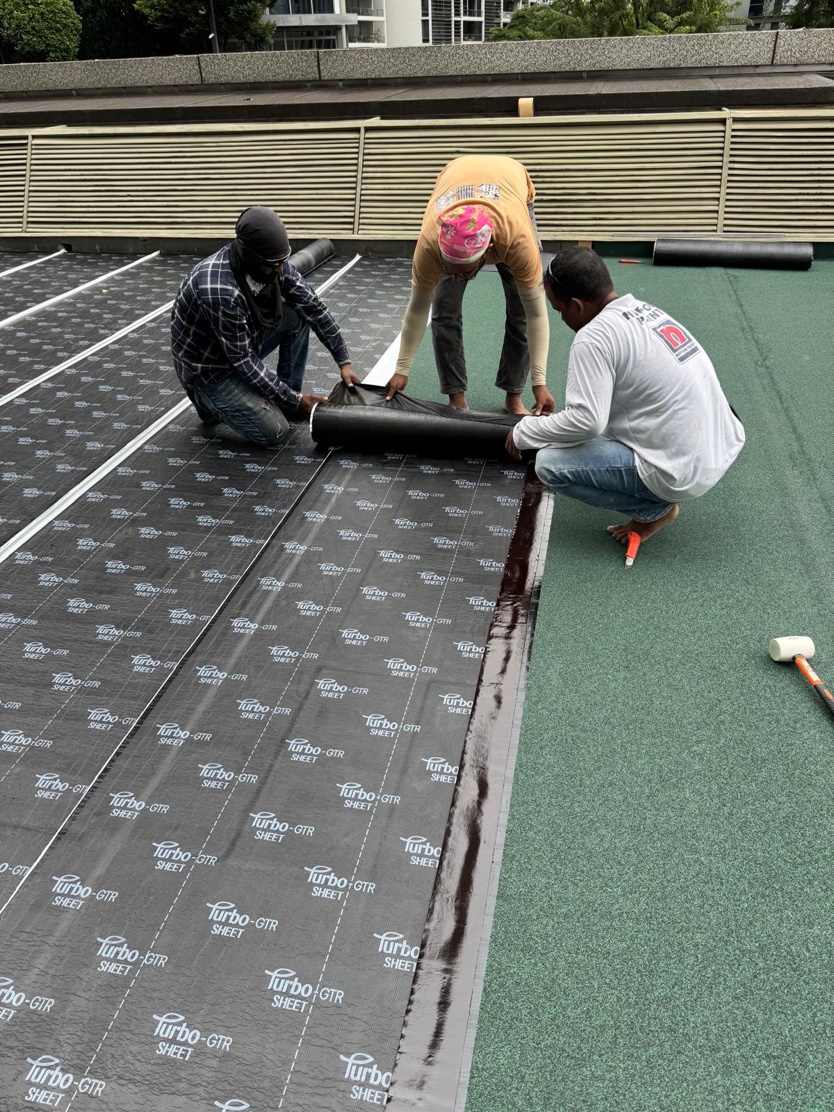 Technician applying NPR liquid waterproofing membrane across a flat commercial rooftop