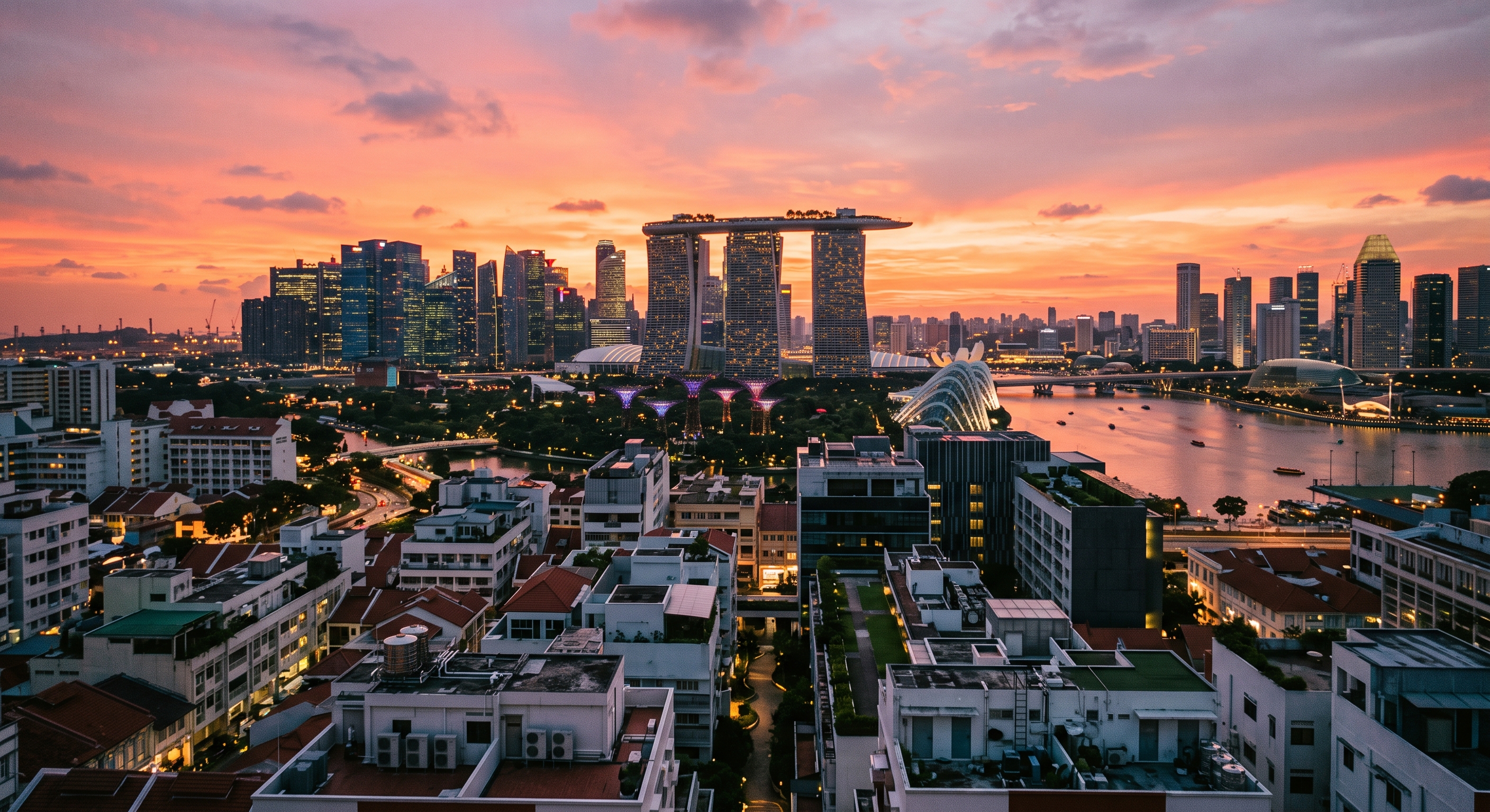 Aerial view of the Singapore skyline and Marina Bay at sunset, with rooftops in the foreground